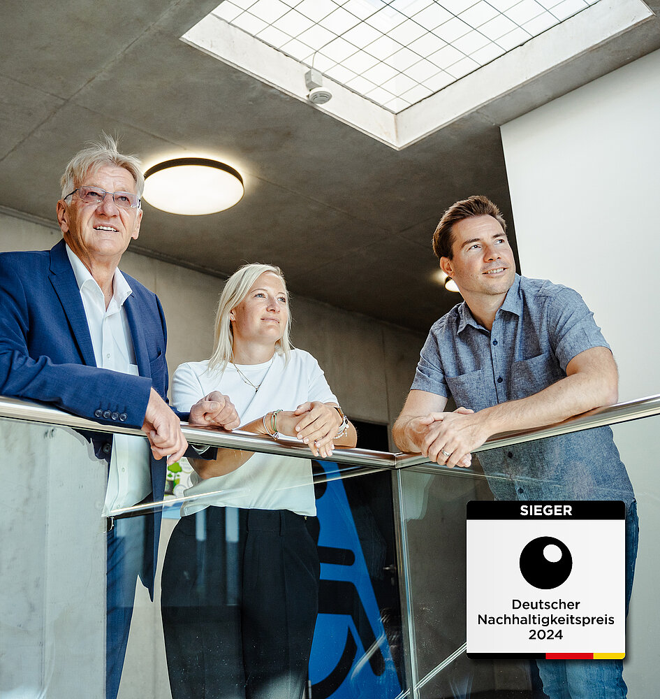 2 Männer und eine Frau lehnen an einem Geländer und blicken in eine Richtung. In der rechten unteren Ecke befindet sich das Sieger-Siegel für den deutschen Nachhaltigkeitspreis 2024.