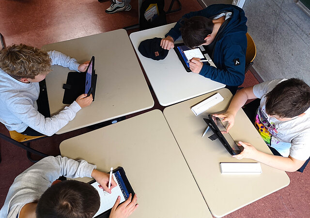 Aufnahme aus der Vogelperspektive, vier Schüler:innen arbeiten in der Schule an ihren iPads.